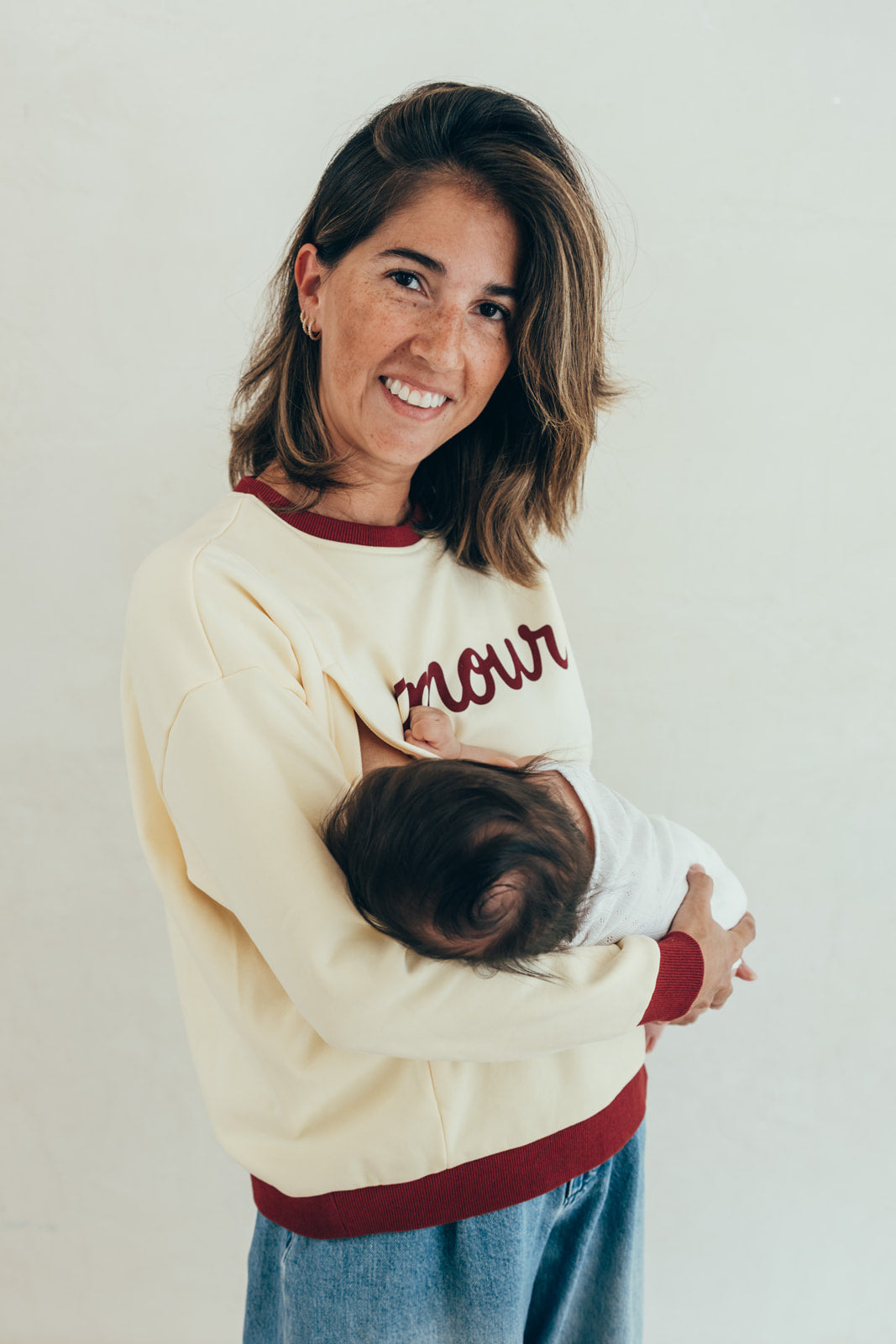 Maman portant le sweat-shirt d'allaitement bicolore Amour 23 Mai Paris, allaitant son bébé au sein grâce au zip d'allaitement discret.