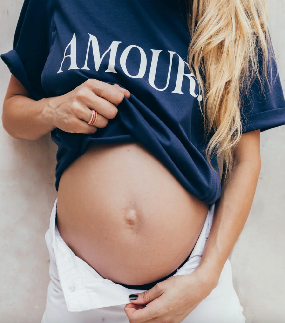 Photo of a pregnant woman pulling up her maternity t-shirt and opening her pants to reveal her round belly.