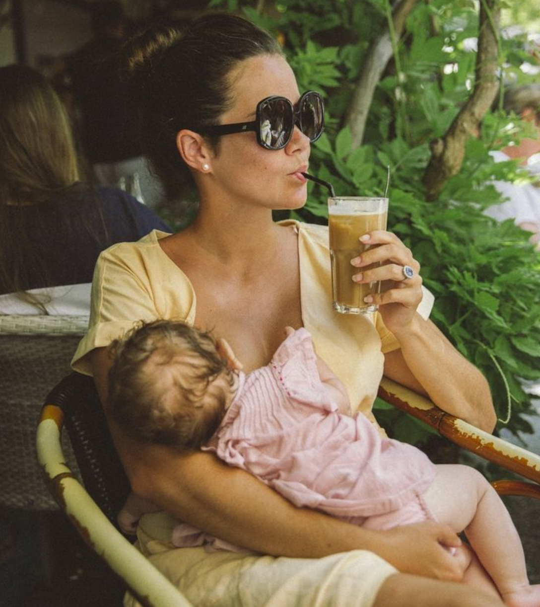 A woman drinking a cocktail while breastfeeding her baby