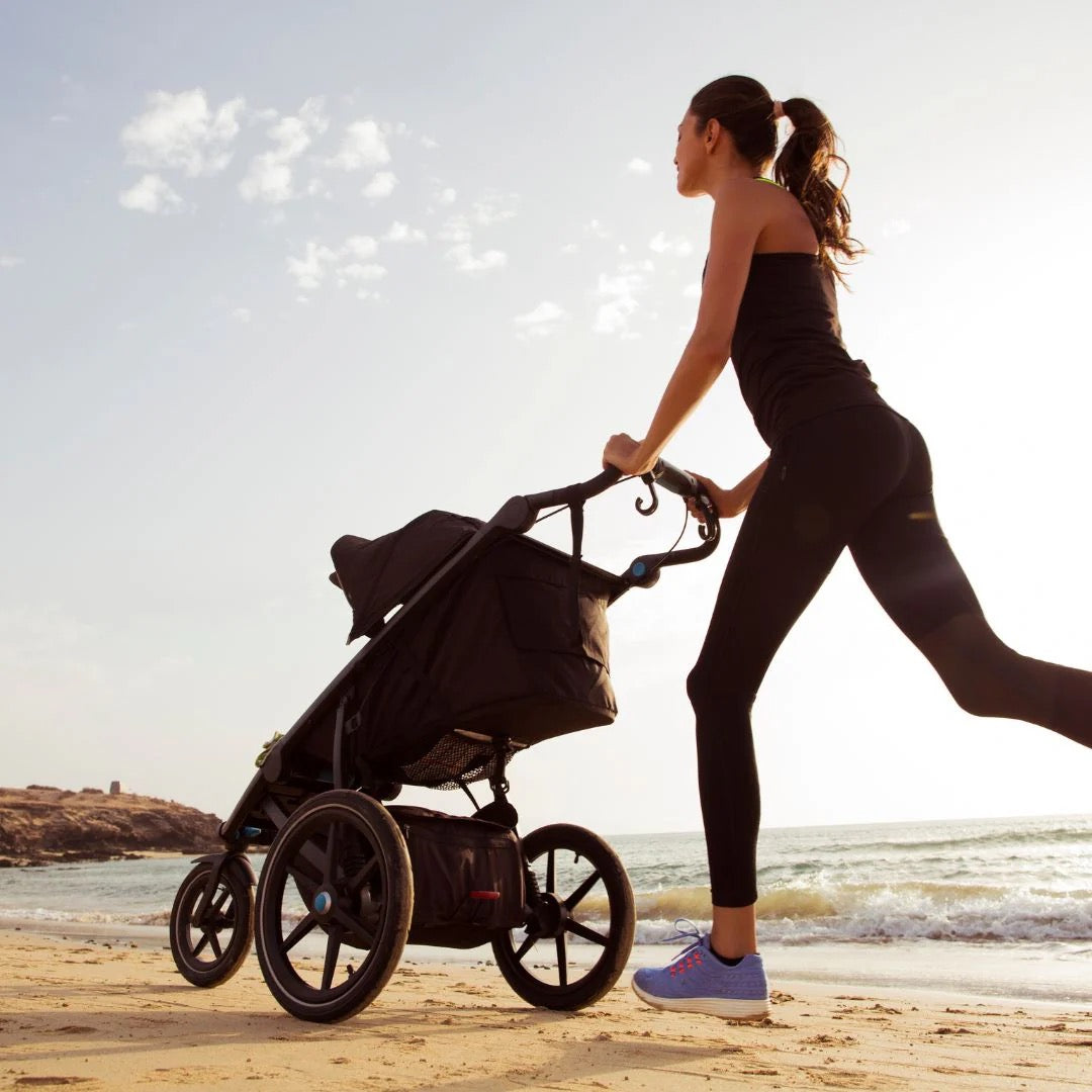 Frau mit Kinderwagen, die am Strand Sport treibt