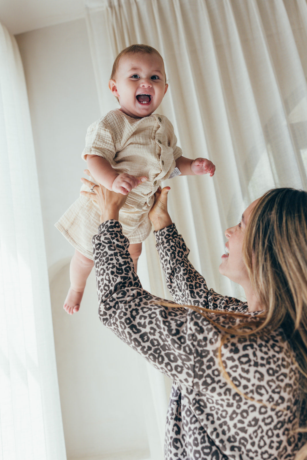 A mom wearing the Leo nursing sweatshirt 23 Mai Paris, lifting her baby up in the air with a smile.