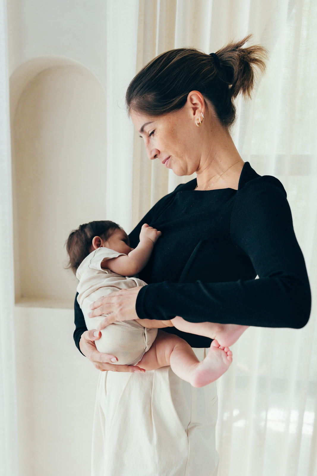 Maman portant le t-shirt d'allaitement noir manches longues ML 23 Mai Paris, allaitant son bébé au sein grâce au zip d'allaitement discret.